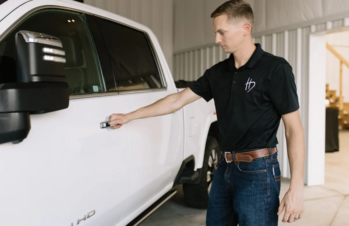 Rusty Hermsmeyer opening the door of a customer's white GMC truck at the Hermsmeyer Detailing shop
